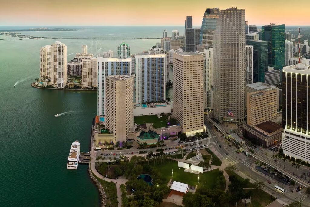 Paisaje urbano de Miami al anochecer, con rascacielos iluminados y reflejos sobre el mar que expresan lujo moderno y energía cosmopolita.