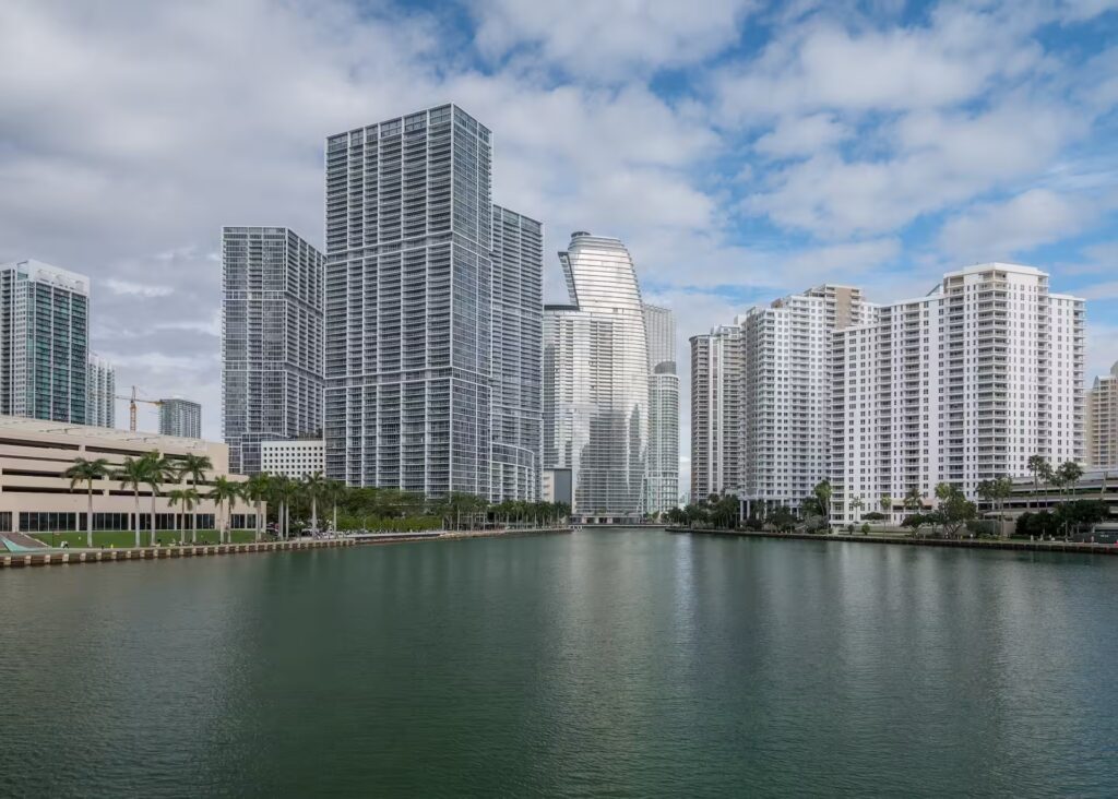 Vista urbana de Brickell, Miami, con rascacielos modernos reflejándose sobre el río y una atmósfera vibrante de vida contemporánea.